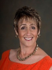 Leslie Canham headshot photo with red shirt and gold necklace and earings